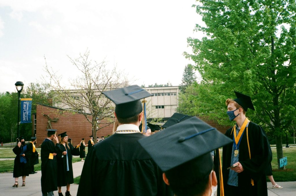 Menschen in akademischer Kleidung stehen tagsüber in der Nähe grüner Bäume